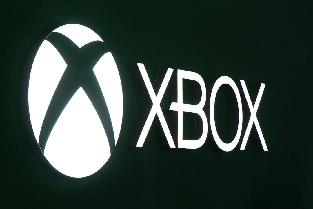 An Xbox controller in front of a screen showing an online feedback forum with posts about layoffs.